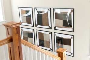 A staircase with a wooden handrail and six framed artworks on the wall above.