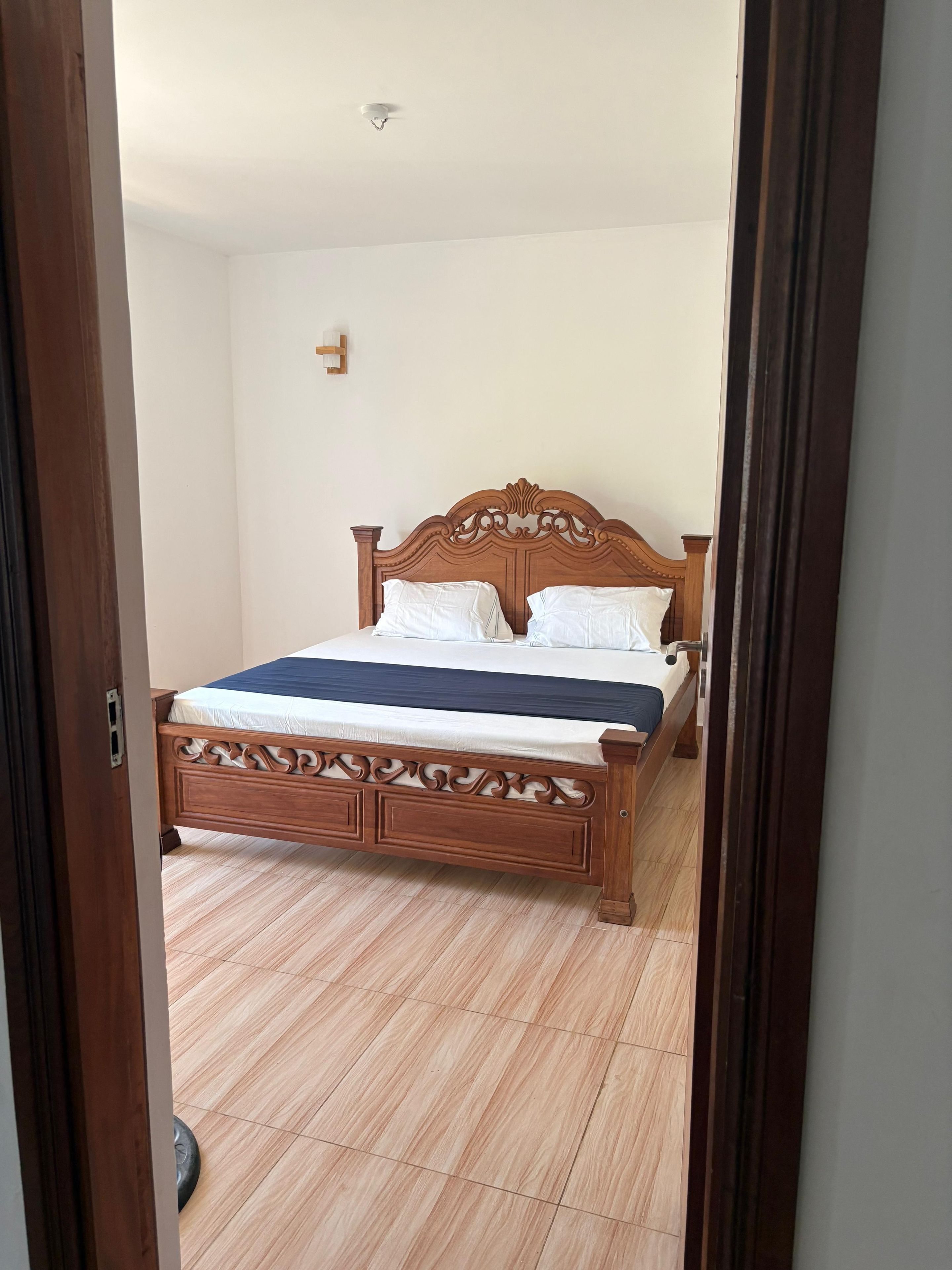 A bedroom with a wooden bed, white bedding, and a light-colored floor.