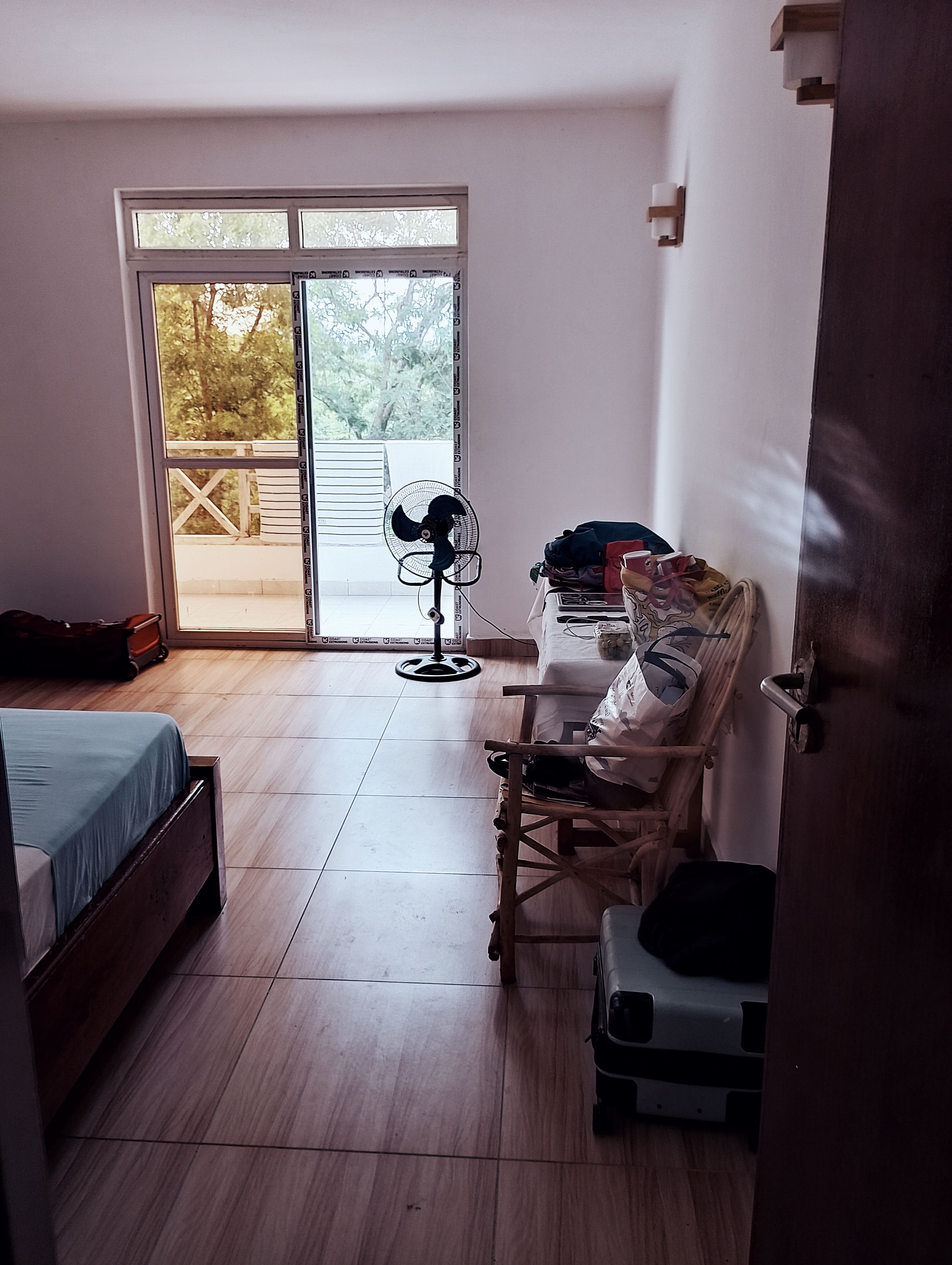 Una habitación con cama, una silla, un ventilador y una maleta.