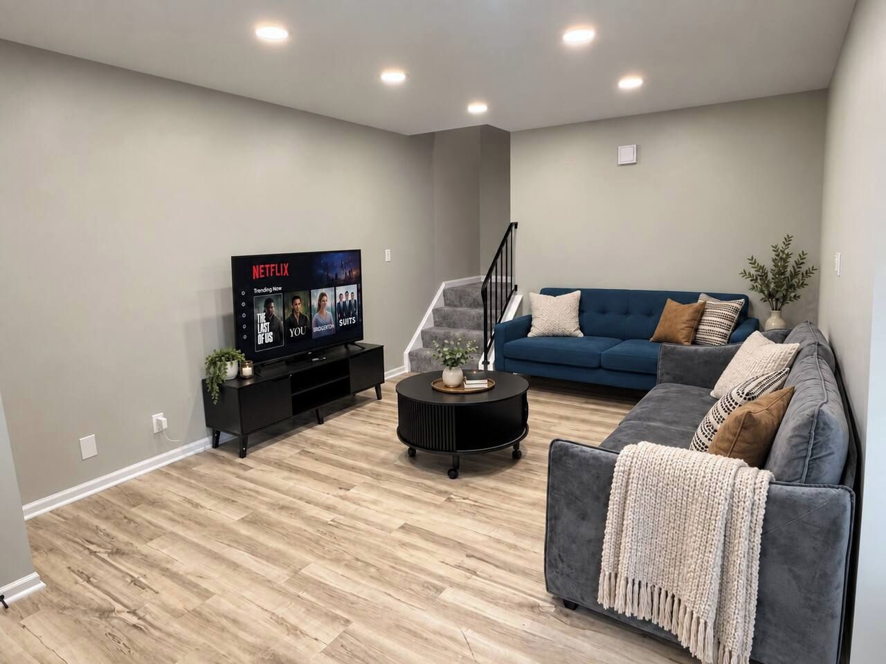 Ein modernes Wohnzimmer mit Fernseher, blauem Sofa, grauem Sessel und einer Treppe.