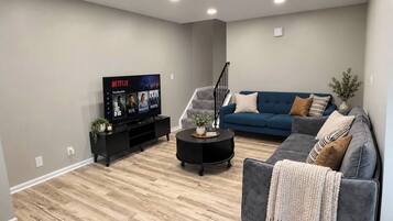 Ein modernes Wohnzimmer mit Fernseher, blauem Sofa, grauem Sessel und einer Treppe.