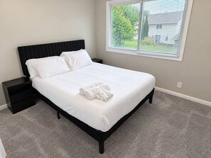 Quarto com cama, mesa de cabeceira e janela com persianas.