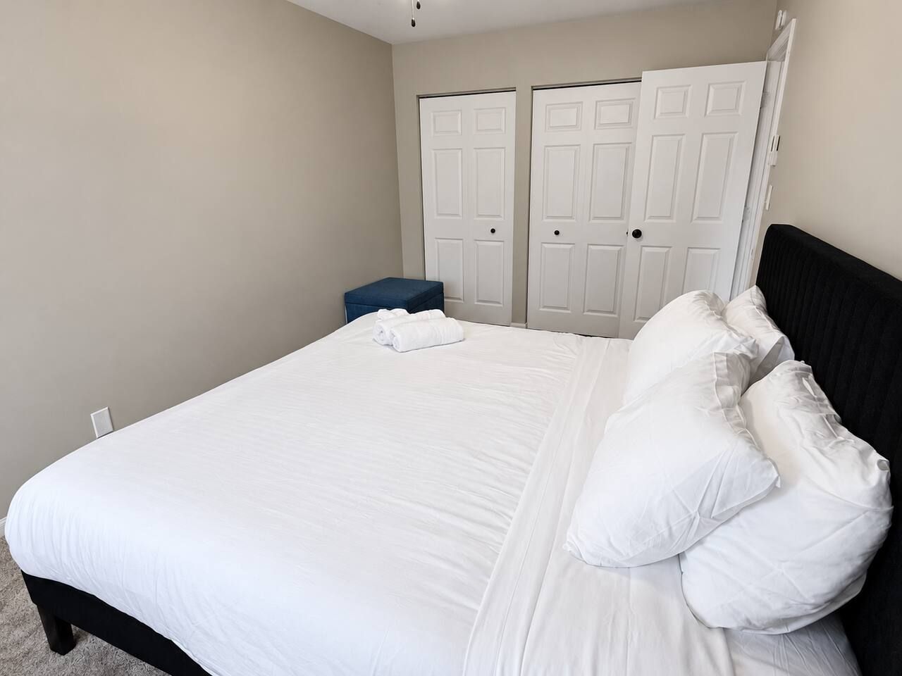 A bedroom with a bed, white pillows, a blue bench, and two white doors.