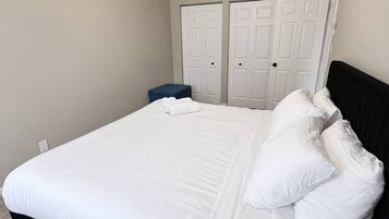 A bedroom with a bed, white pillows, a blue bench, and two white doors.
