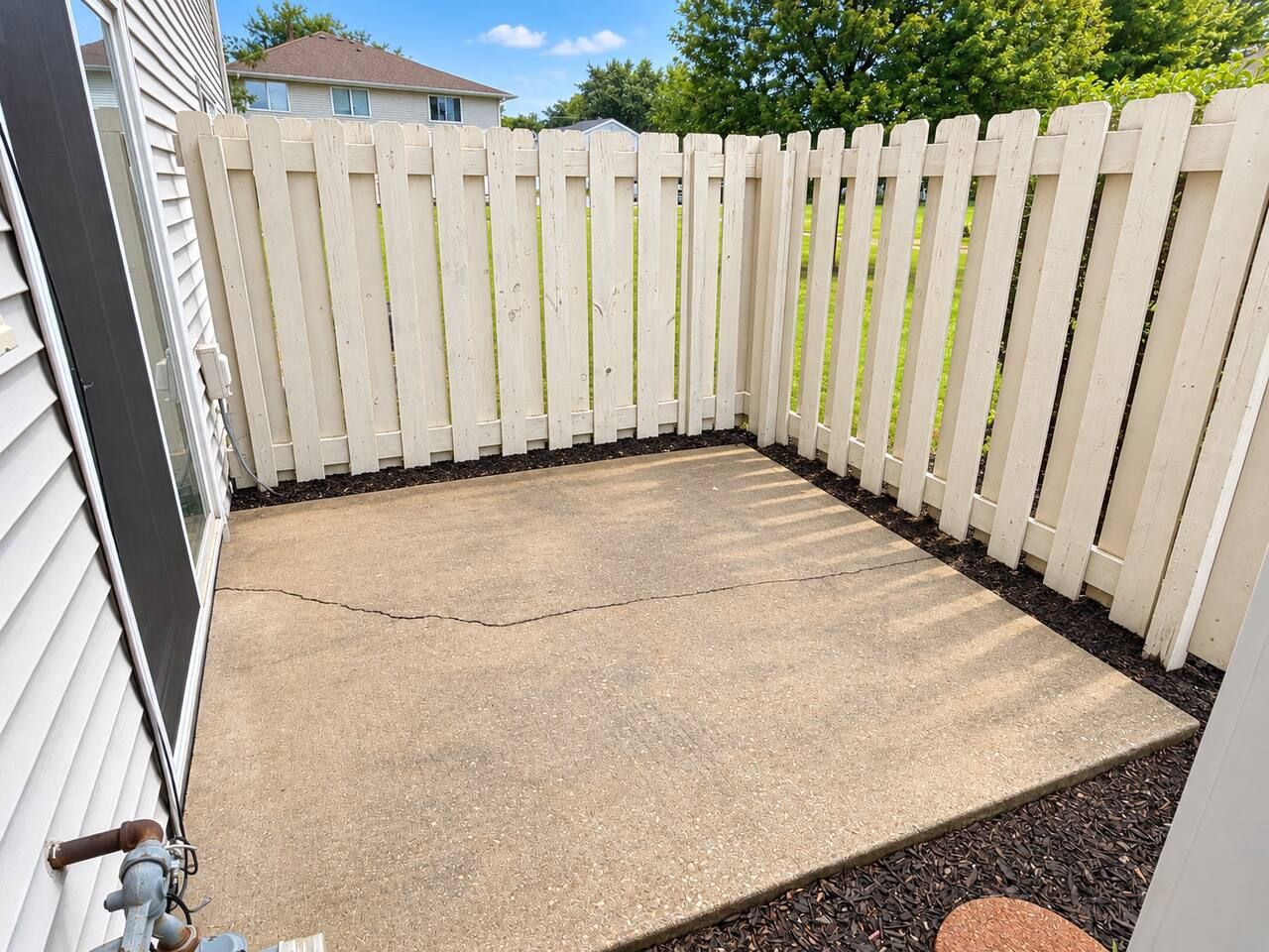 A concrete patio area enclosed by a white picket fence, with a visible crack in the concrete.