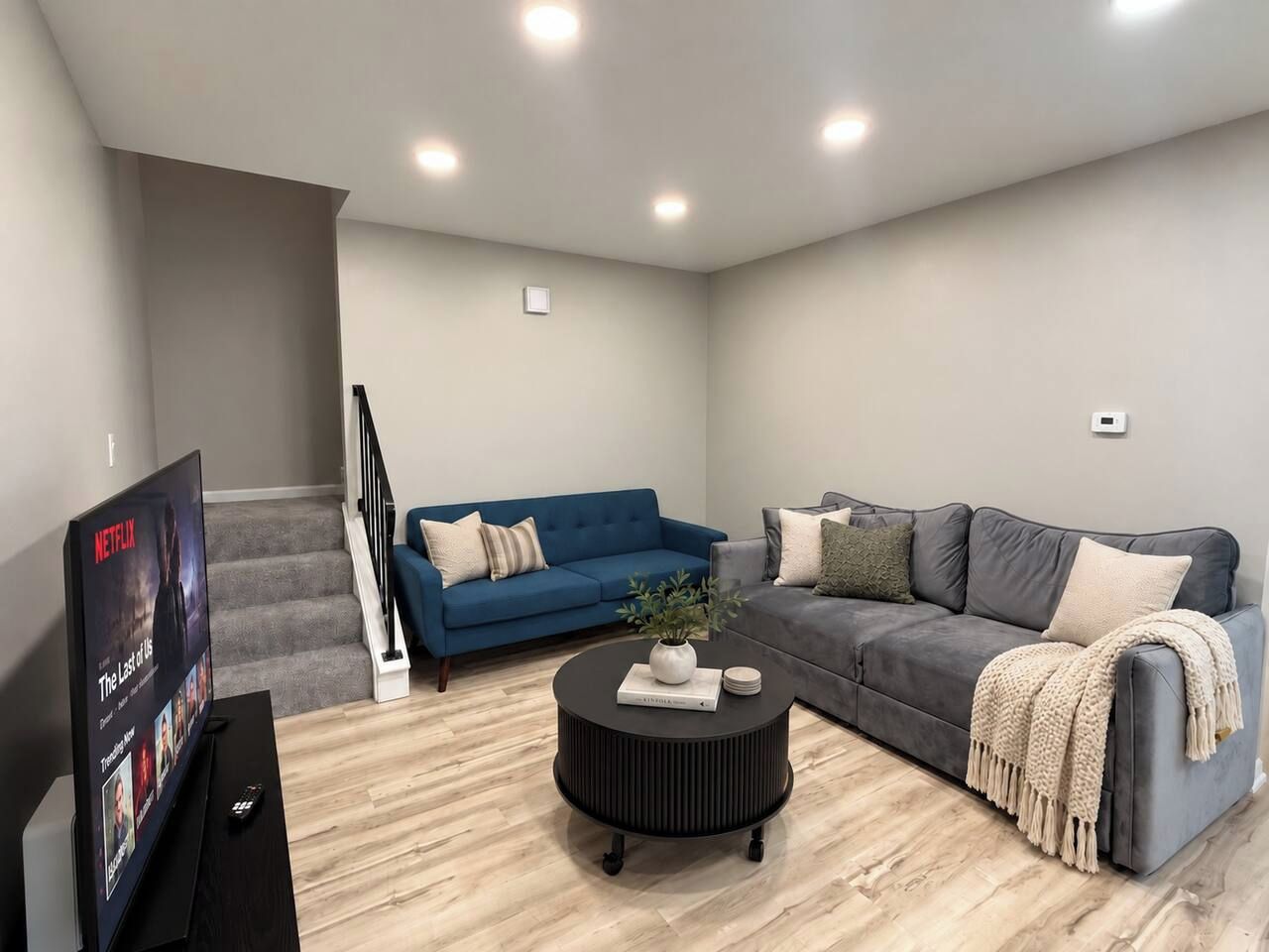 Uma sala de estar moderna com televisão de tela plana, dois sofás, uma mesa de centro e uma escada.