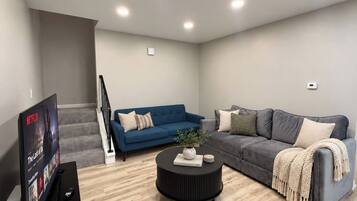 Uma sala de estar moderna com televisão de tela plana, dois sofás, uma mesa de centro e uma escada.