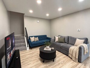 Uma sala de estar moderna com televisão de tela plana, dois sofás, uma mesa de centro e uma escada.