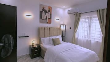 Une chambre à coucher moderne, équipée d’un lit, d’une table de chevet, d’une lampe fixée au mur et d’un ventilateur de plafond.