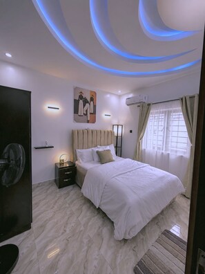 A modern bedroom with a bed, bedside table, wall-mounted light, and a ceiling fan. - Lyton CriB (Abeokuta)