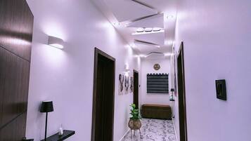 A hallway with a marble floor, recessed lighting, a wall-mounted clock, and a small plant.