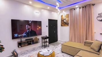 A modern living room with a flat-screen TV, a sofa, a coffee table, and a decorative ceiling light.
