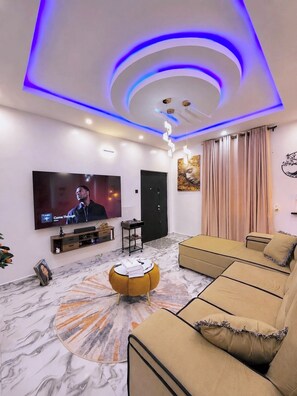 Een moderne woonkamer met een flatscreen televisie, een bank, een salontafel en een decoratieve plafondlamp.