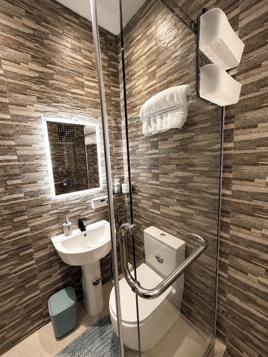Un baño moderno con cabina de ducha de vidrio, un lavamanos blanco y un inodoro.