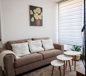 A living room with a brown sofa, three white cushions, a small round table, and a painting on the wall. - Torre Manuel Rodriguez by Domus Travels (Santiago)