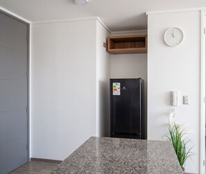 A kitchen with a granite countertop, a black refrigerator, a wooden shelf, a wall clock, and a potted plant. - Torre Manuel Rodriguez by Domus Travels (Santiago)