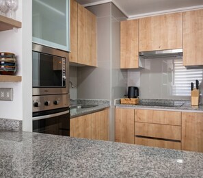 A modern kitchen with granite countertops, stainless steel appliances, wooden cabinets, and a built-in microwave. - Torre Manuel Rodriguez by Domus Travels (Santiago)