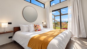A hotel room with a large bed, a round mirror on the wall, and a view of the outdoors through a large window. - Natura Lodge by Villa Alejandro (Bajo Boquete)