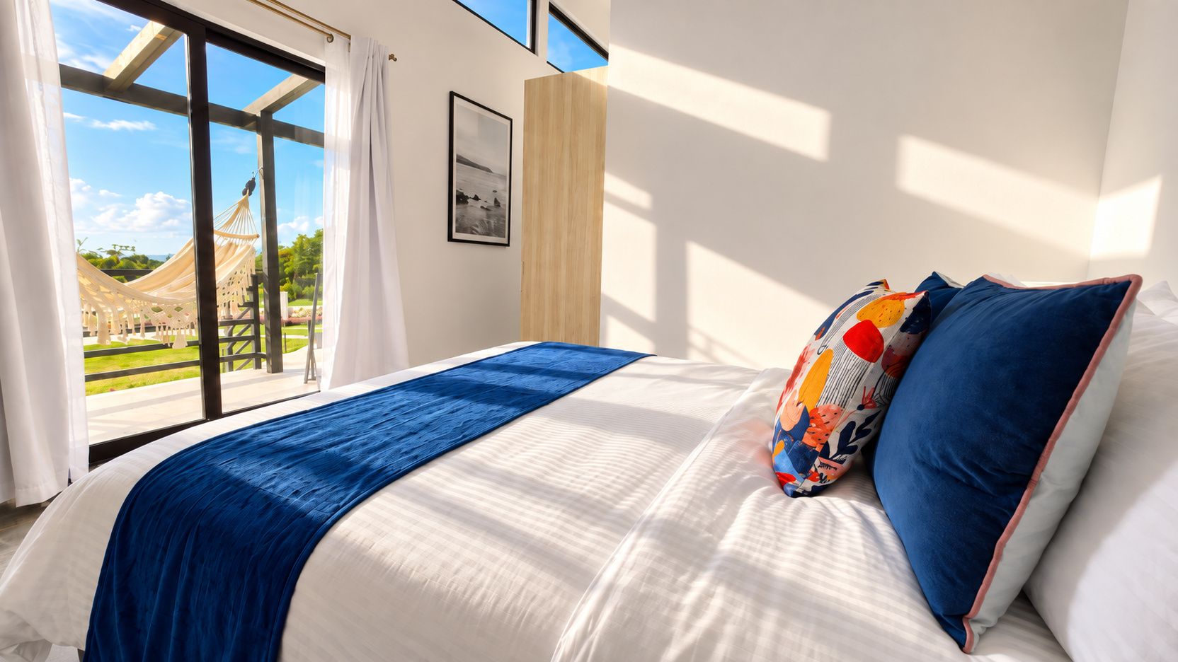 A hotel room with a large bed, a view of a garden, and a hammock outside the window.