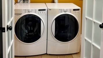 A pair of front-loading washing machines in a laundry room with a yellow wall and a white door.