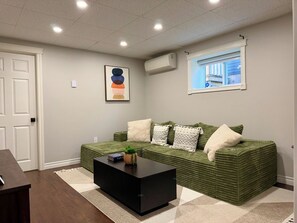 A living room with a green sofa, a black coffee table, and a framed abstract art piece on the wall.