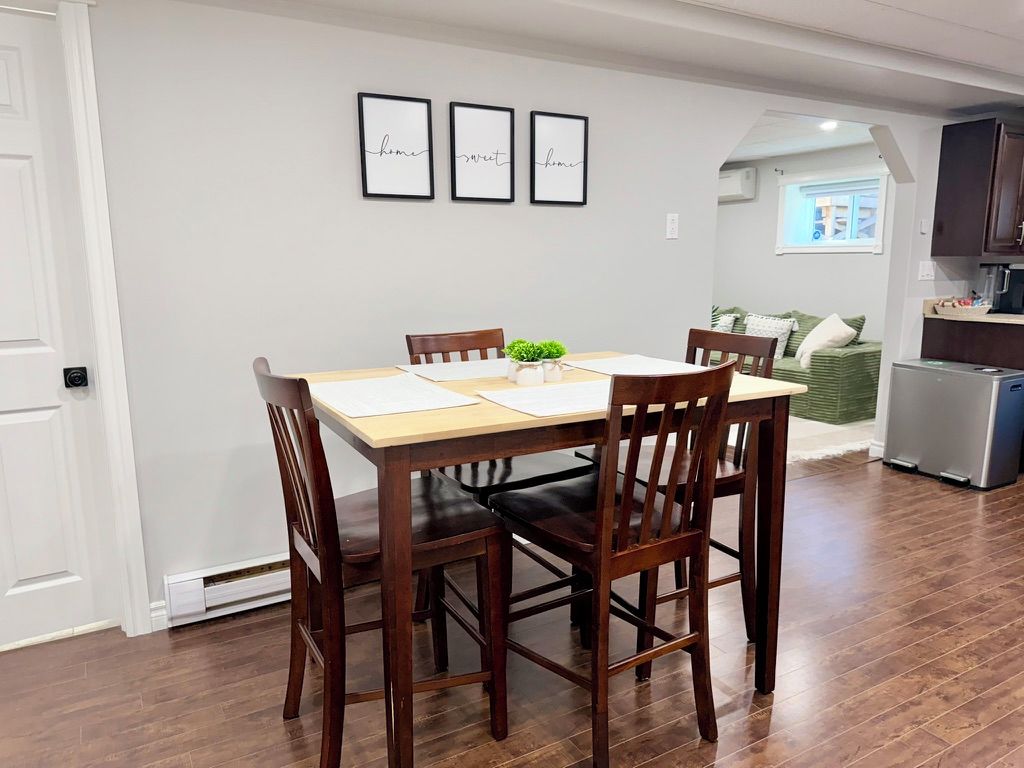 A dining area with a wooden table and chairs, a small plant on the table, and a kitchen in the background.
