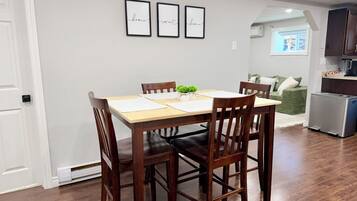 A dining area with a wooden table and chairs, a small plant on the table, and a kitchen in the background.