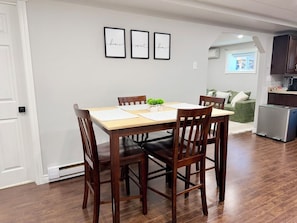 A dining area with a wooden table and chairs, a small plant on the table, and a kitchen in the background.
