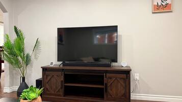 A living room with a flat-screen TV on a wooden entertainment center, a potted plant, and a book on a coffee table.