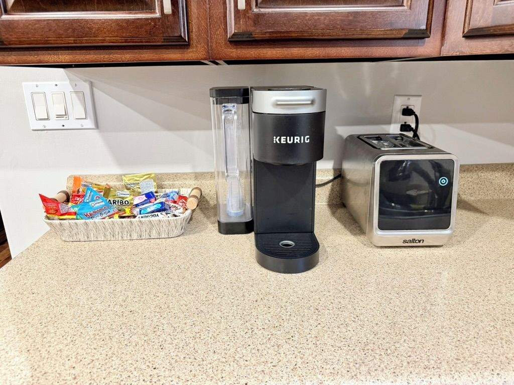 A kitchen counter with a Keurig coffee maker, a toaster, and a basket of snacks.