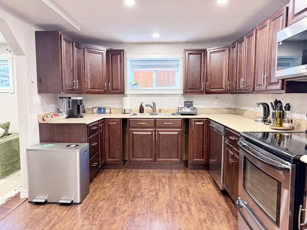 A kitchen with dark wooden cabinets, a stainless steel refrigerator, a dishwasher, and a stove.
