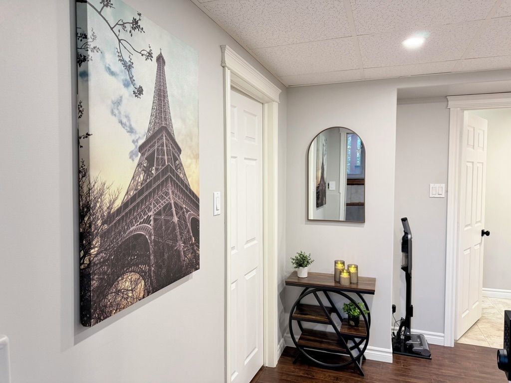 A hallway with a painting of the Eiffel Tower, a console table with candles, and a vacuum cleaner.