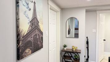 A hallway with a painting of the Eiffel Tower, a console table with candles, and a vacuum cleaner.