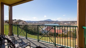 A balcony with a green railing overlooking a town and mountains.