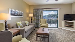 Quarto de hotel com sofá, poltronas, mesa de centro, televisão e varanda com vista.