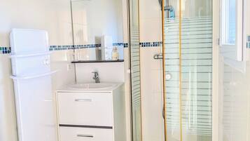 Een badkamer met toilet, wastafel, kastruimte en een douchecabine met glazen wanden.