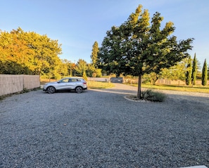 Une allée de gravier mène à une voiture garée, avec un arbre au premier plan.