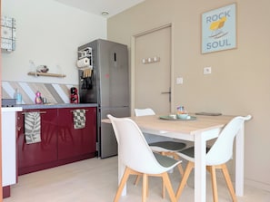 Cocina compacta con refrigerador, cafetera y comedor con mesa y sillas.
