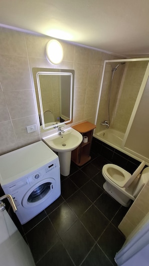A compact bathroom with a washing machine, a sink, a toilet, and a shower.