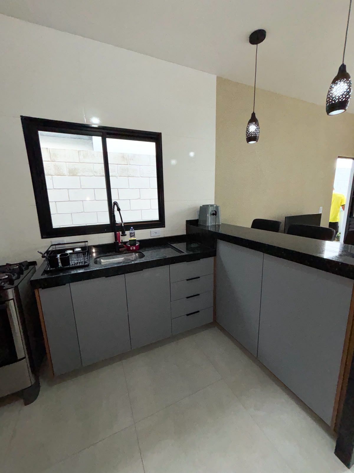 A kitchen with a black countertop, a window with a black frame, a sink, and a stove.