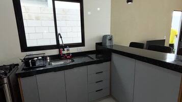 A kitchen with a black countertop, a window with a black frame, a sink, and a stove.