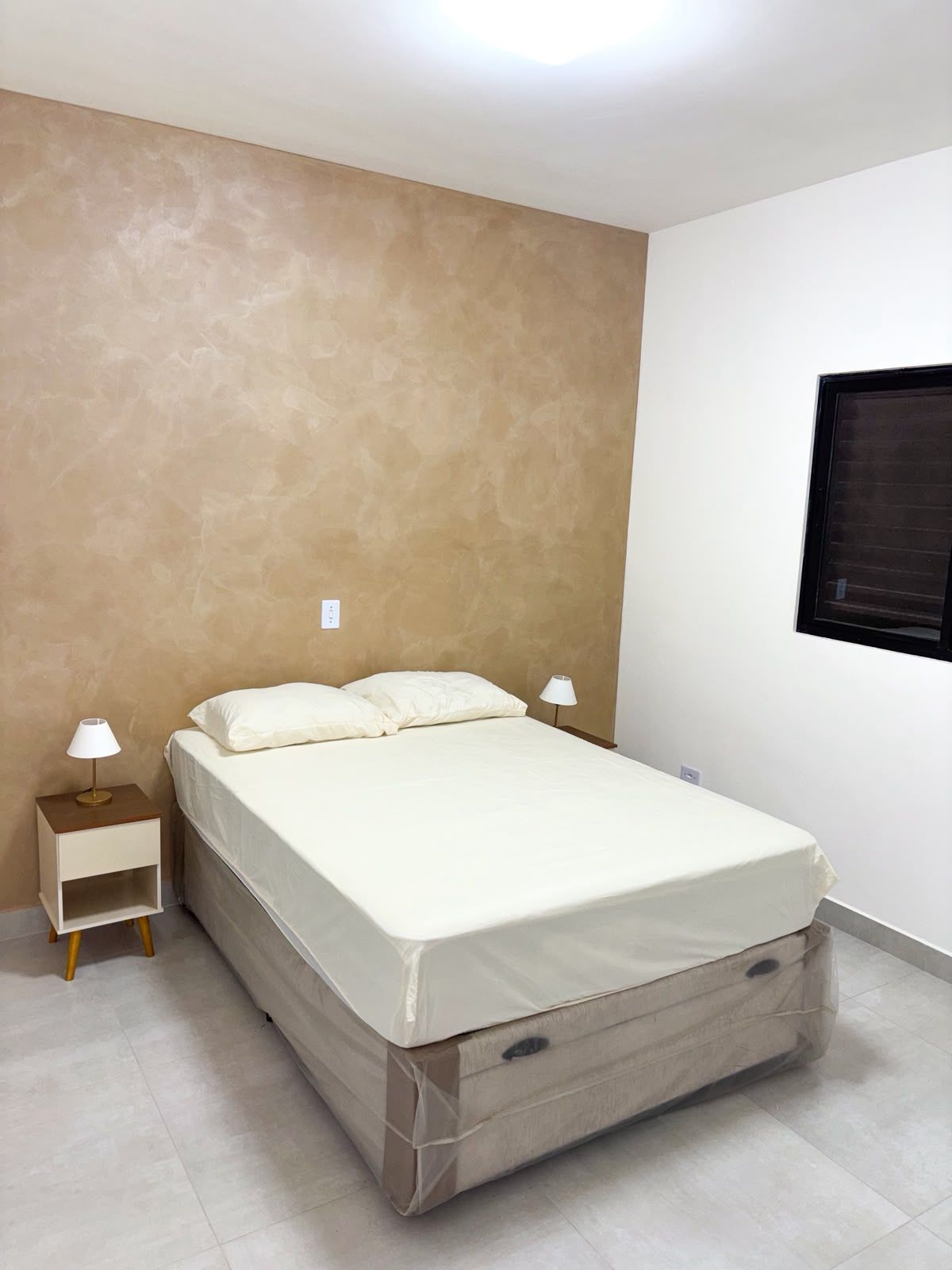 Quarto com cama, duas mesas de cabeceira e uma janela.