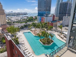 A rooftop pool with palm trees, surrounded by lounge chairs and a cityscape view. - Dreamy 1BR | Skyline Balcony City Views+ Pool, Spa, Gym (Miami)