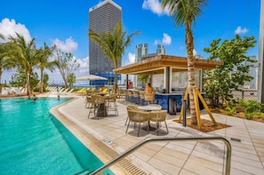 A rooftop pool area with lounge chairs, a bar, and a view of a tall building. - Dreamy 1BR | Skyline Balcony City Views+ Pool, Spa, Gym (Miami)
