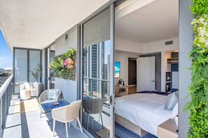 A modern hotel room with a balcony, a bed, a seating area with chairs, and a wall-mounted plant. - Dreamy 1BR | Skyline Balcony City Views+ Pool, Spa, Gym (Miami)