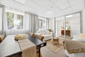 A modern living room with a large table, a sofa, and a coffee table. There is a window with curtains, a mirror, and a dresser with a mirror. - Vrbo Property (Montpon-Ménestérol)