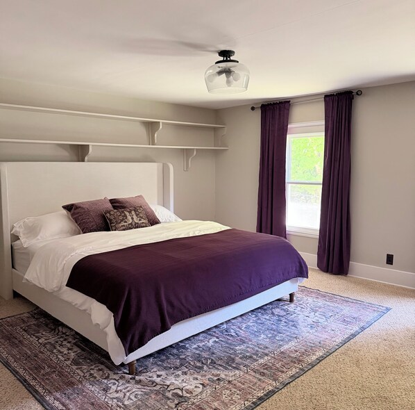A bedroom with a bed, a ceiling fan, a window with curtains, and a patterned rug.