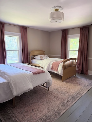 A bedroom with two beds, a large window, and a ceiling light fixture.