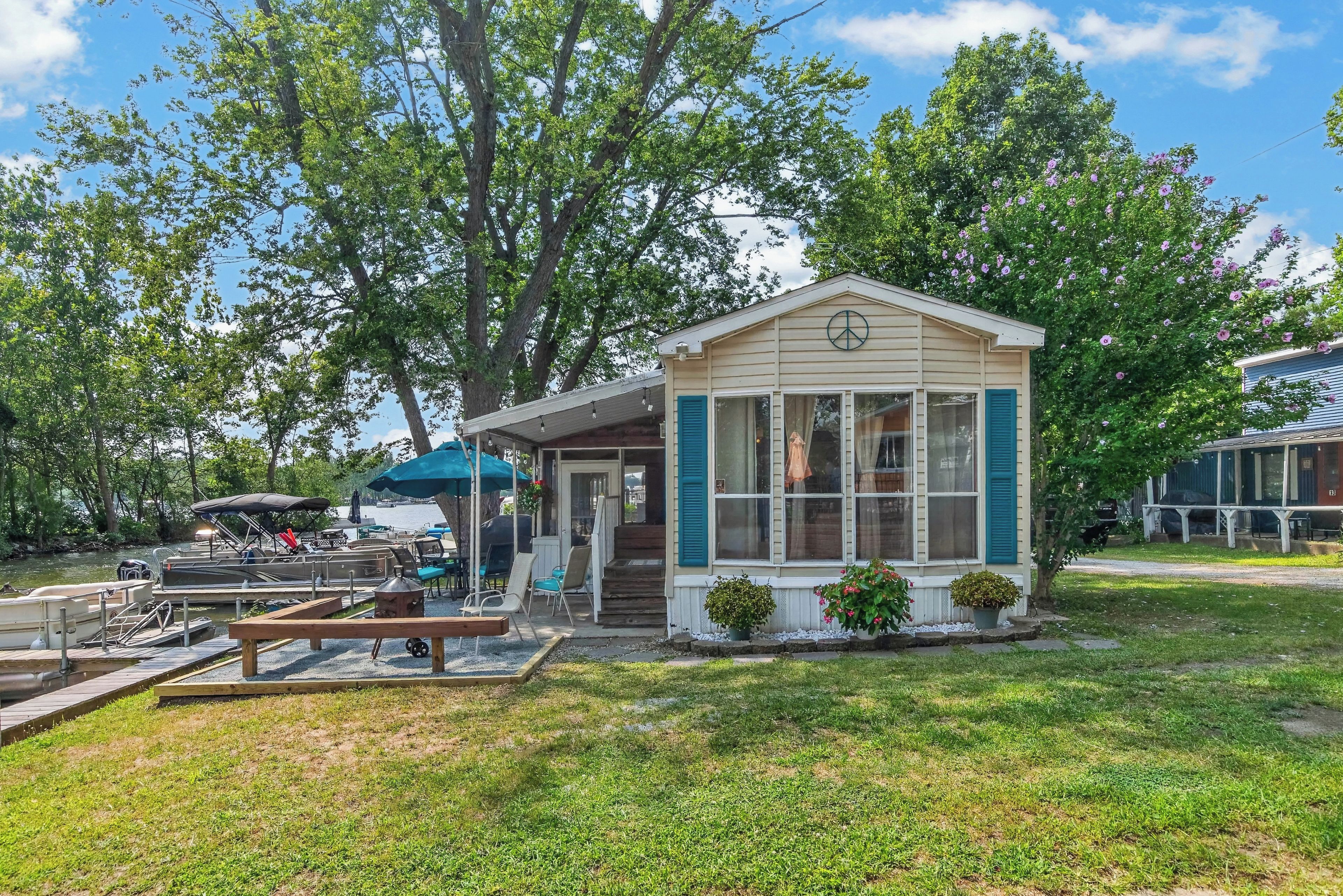 Une petite maison avec un porche, un espace extérieur couvert aménagé en coin salon et un quai avec des bateaux.