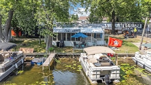Een vakantiehuis aan het meer, met een steiger, een overdekte boot en een terras.
